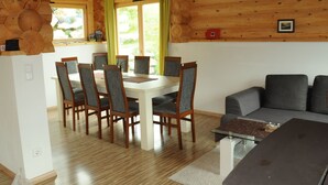 Interior de uma cabana de madeira com uma mesa de jantar, cadeiras, um sofá e uma mesa de centro de vidro.