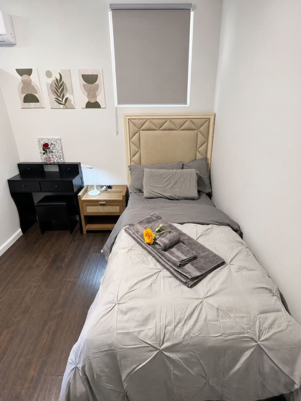 A bedroom with a bed, a desk, a nightstand, and a window.