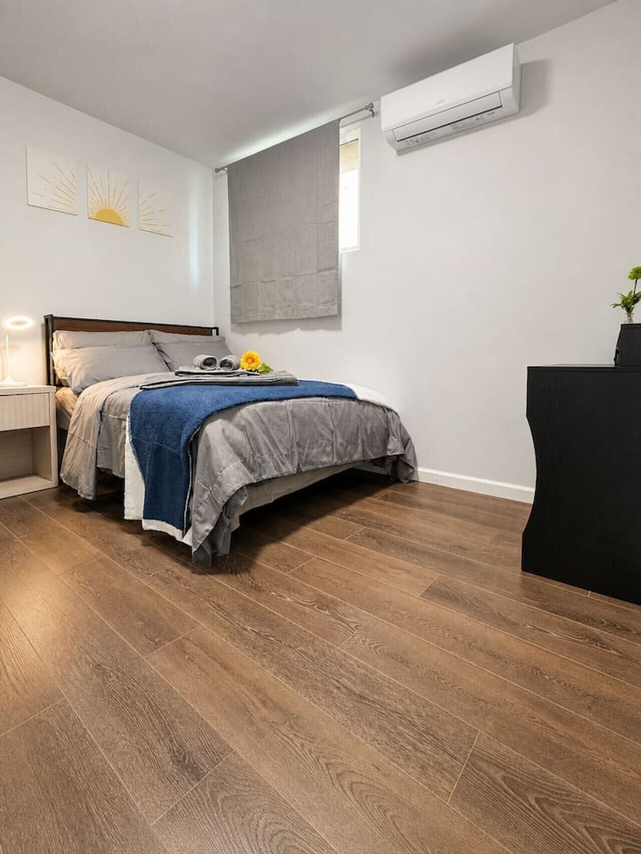 A bedroom with a bed, bedside table, lamp, and an air conditioning unit.
