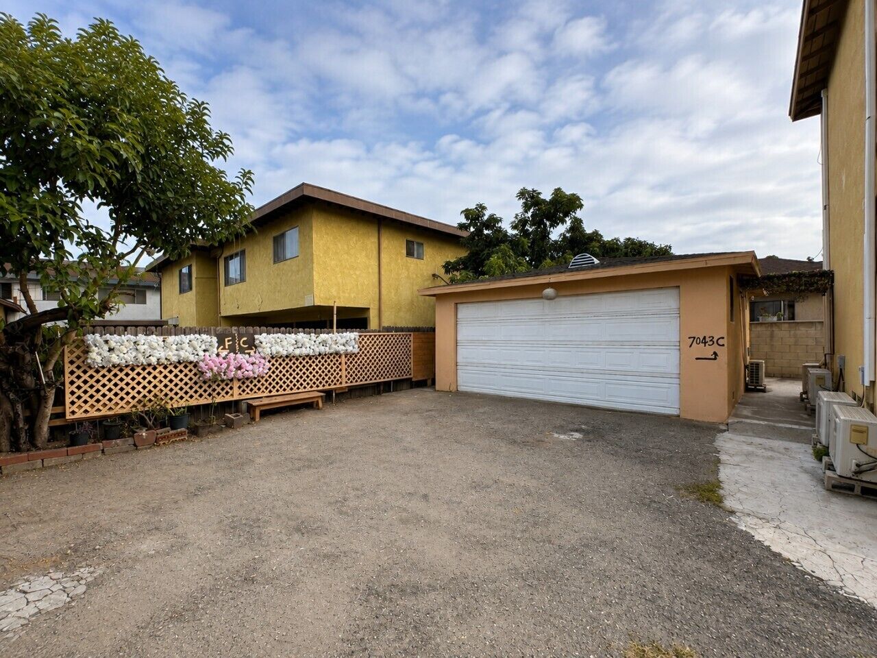 A residential property with a garage, a fenced area with potted plants, and a clear sky.