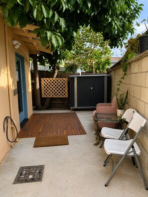 A patio area with a wooden deck, a metal chair, a table, and a black storage shed.