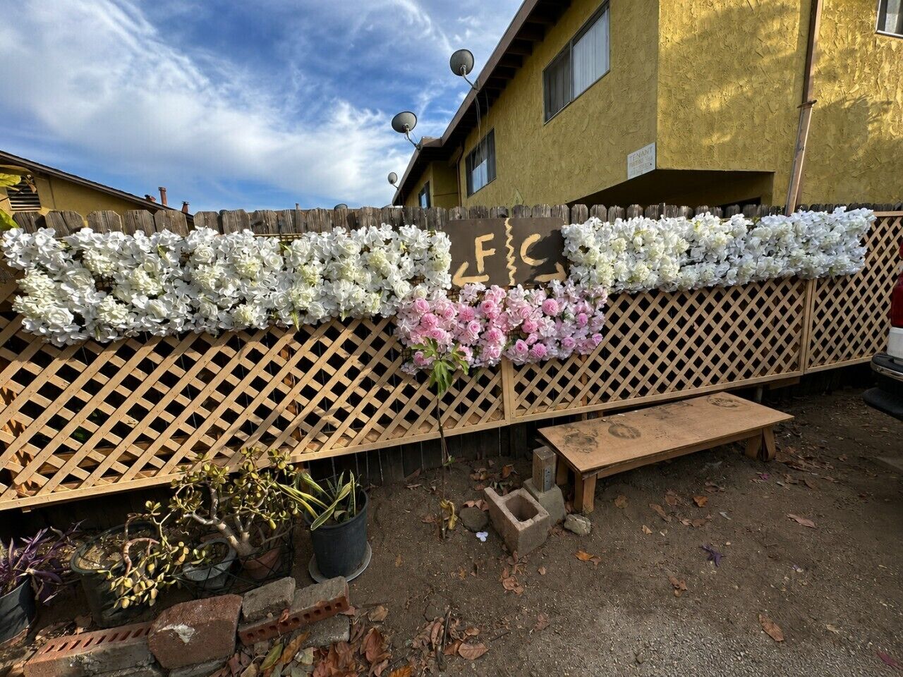 A wooden fence with a floral arrangement, a bench, and potted plants.
