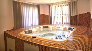 Un jacuzzi grande y rectangular con borde de azulejos, ubicado en una habitación con techo alto e iluminación empotrada.