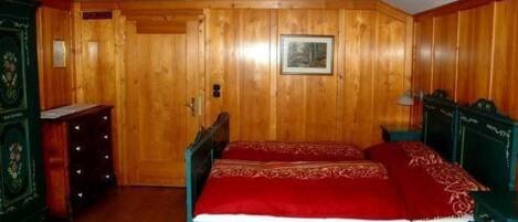 Een kamer met houten wanden, een bed met rode beddengoed en een kledingkast met lades.