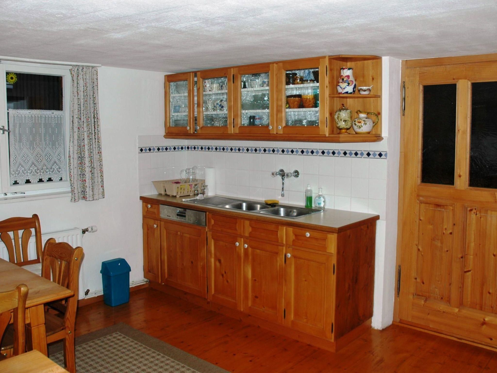 Une cuisine avec des meubles de rangement en bois, un évier et une fenêtre avec des rideaux.