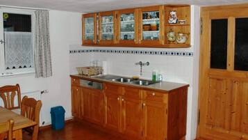 Une cuisine avec des meubles de rangement en bois, un évier et une fenêtre avec des rideaux.