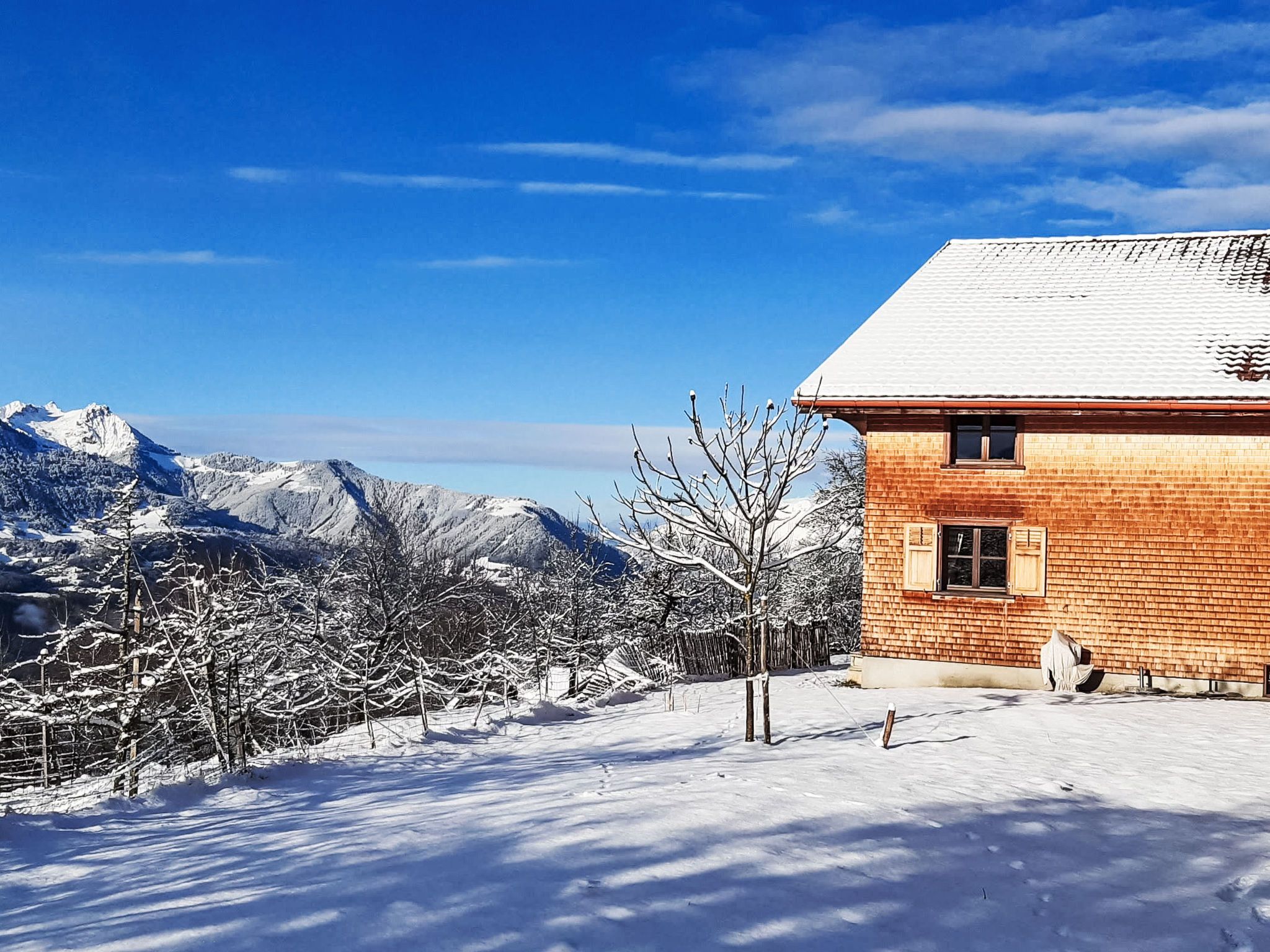 A snow-covered landscape with a wooden house and mountains in the background.