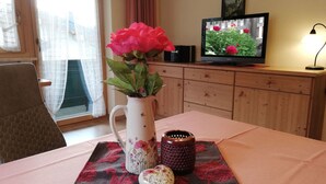Een kamer met een houten kast, een televisie, een vaas met bloemen en een tafel met een placemat.