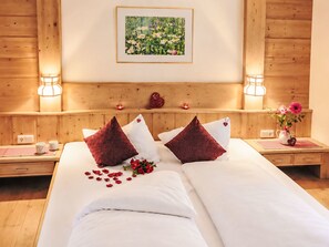 A hotel room with a wooden headboard, a framed floral painting, two bedside tables with lamps, and a bed with white linens and red pillows. - in Wildermieming by Interhome (Wildermieming)