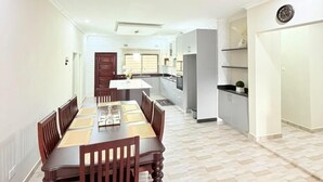 Un vaste espace de salle à manger avec une longue table et des chaises en bois, une cuisine à l’arrière-plan et un aménagement intérieur moderne.