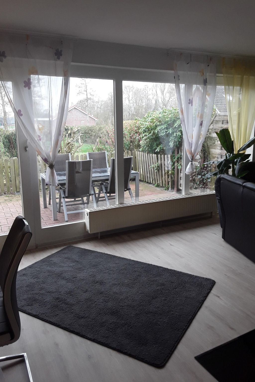 A living room with a large window, a black rug, and a wooden floor.