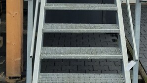 Metallinen portaikko, jossa on metallinen kaide, johtaa ylös rakennuksen sisäänkäynnille.