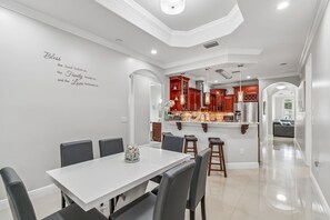 A modern kitchen with red cabinets, a white dining area with a table and chairs, and a decorative wall with a quote. - 1 block from Stadium, Minutes to airport & downtown, King beds, Jetted Bathtub (Tampa)