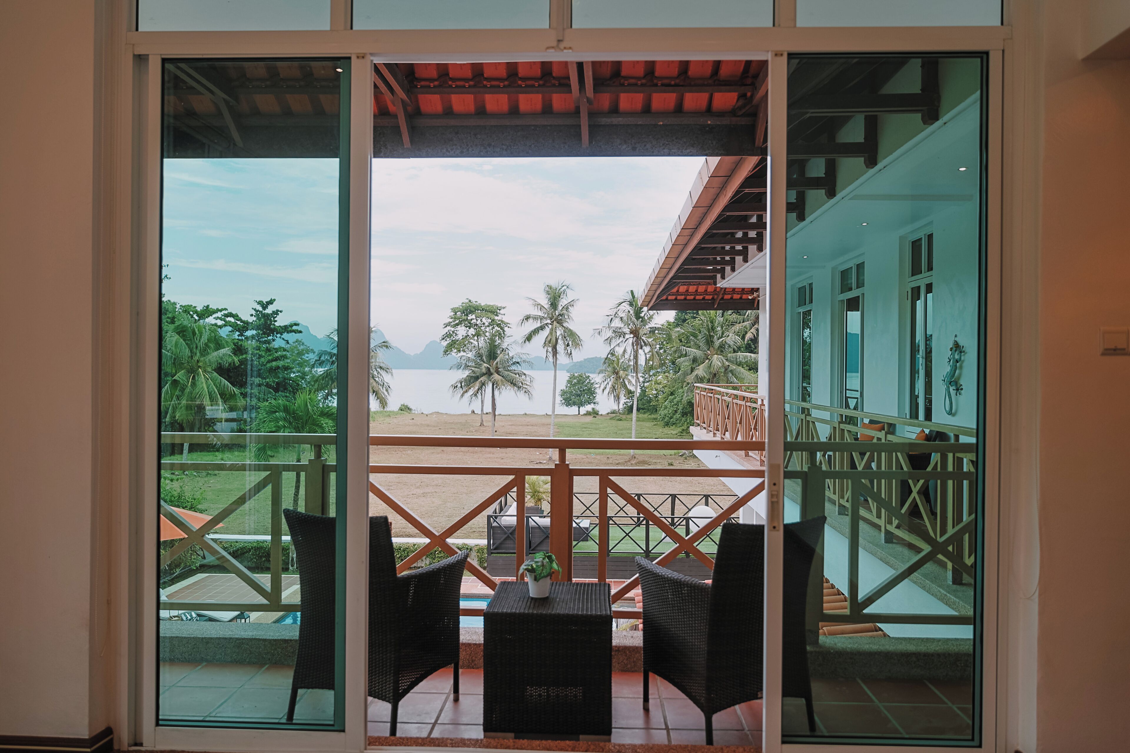 A balcony with wicker furniture and a view of a beach and palm trees.