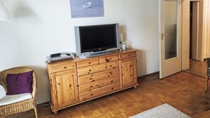 Una stanza con un armadio in legno, una televisione, una sedia in vimini e una porta.