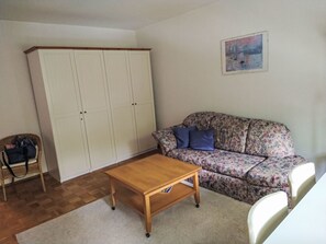 Una habitación con una mesa de madera, un sofá floral, un armario blanco y una silla de mimbre.