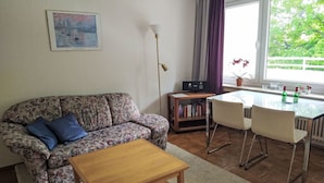 Un soggiorno con un divano, un tavolino, un mobile TV con libri e un tavolo da pranzo con sedie.