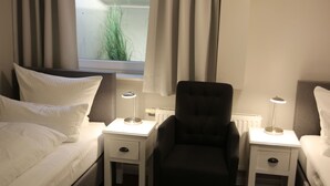 Habitación de hotel con cama, dos mesitas de noche con lámparas, una silla y una ventana con cortinas.