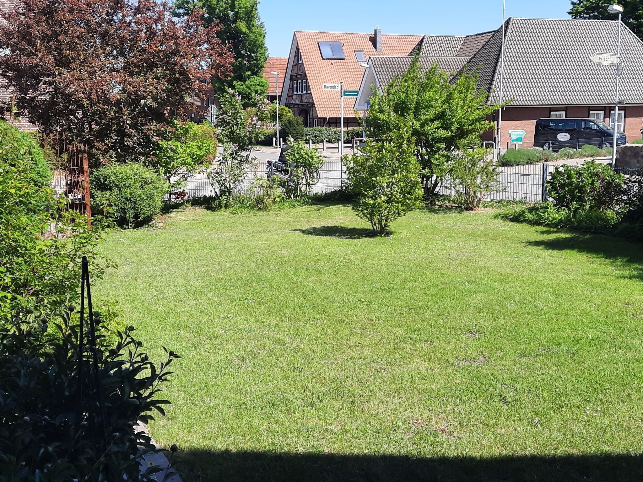 Eine Rasenfläche mit Zaun, Bäumen und einem Gebäude mit Ziegeldach.