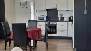 Una cocina compacta con microondas, estufa y alacenas. Hay una mesa de comedor con sillas y un mantel rojo.