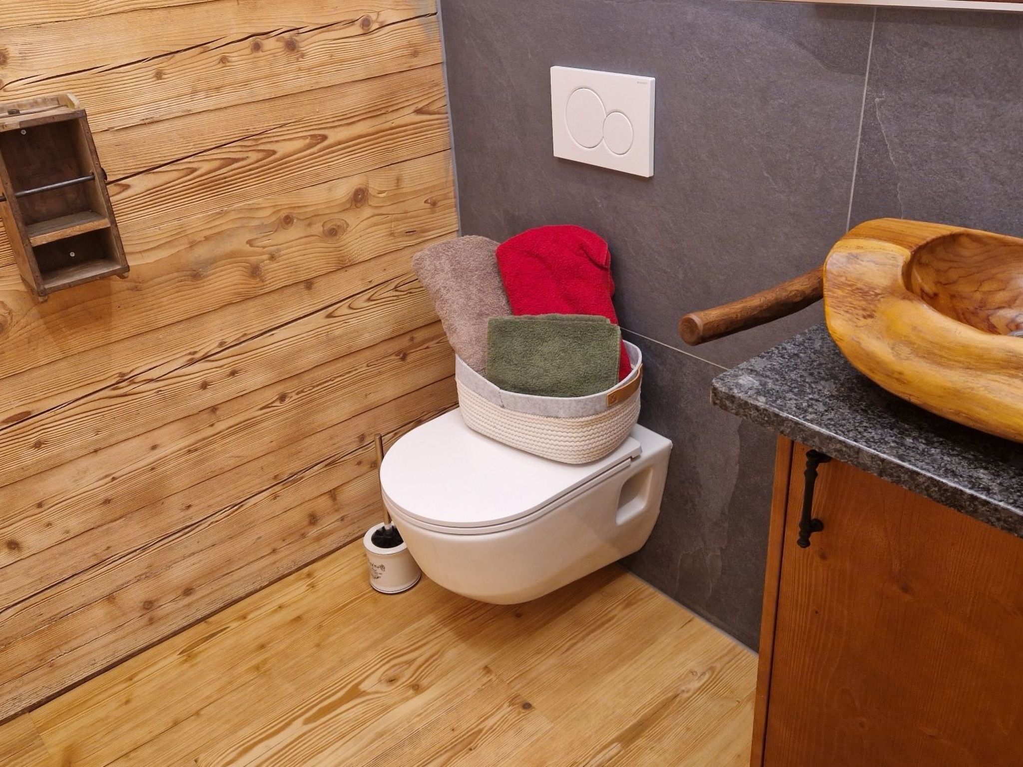 Une petite salle de bain avec un plancher en bois, des toilettes blanches, un petit lavabo et un meuble en bois.