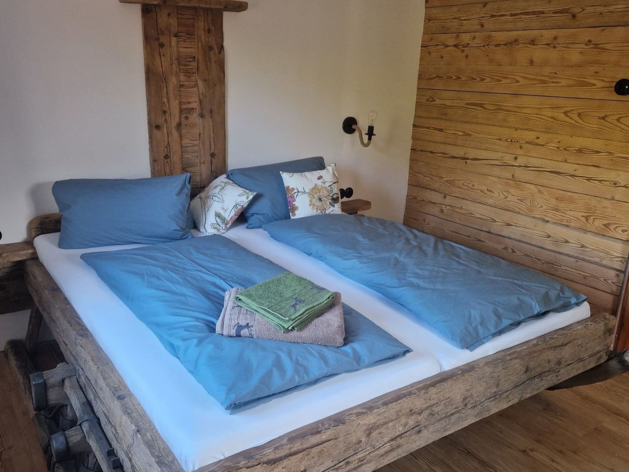 Een bed met blauw beddengoed, een houten hoofdbord en een nachtkastje met een lamp.