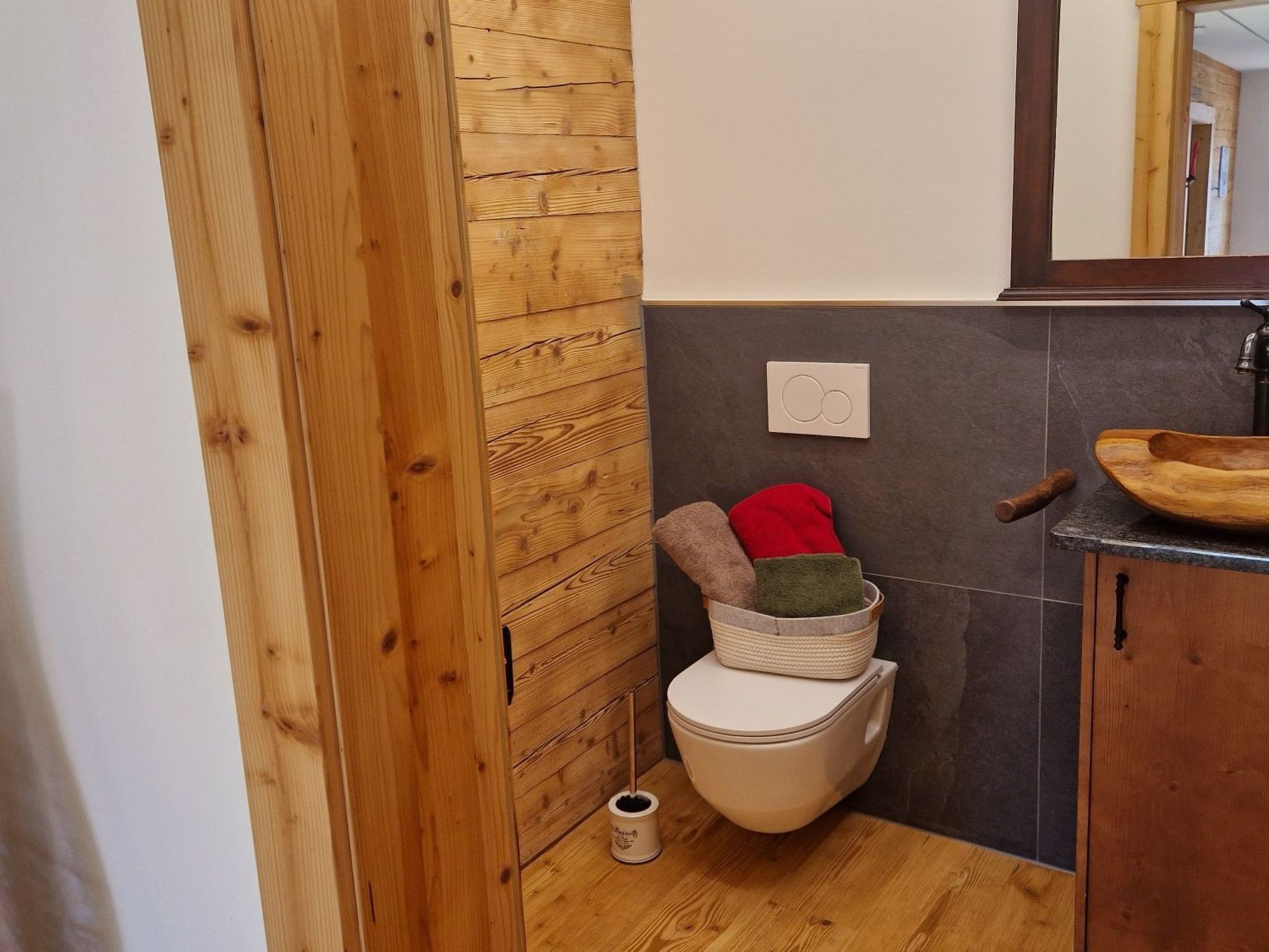 A bathroom with a wooden wall, a toilet, a small trash bin, and a wooden basin on the countertop.
