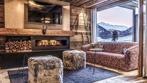 Una sala de estar acogedora con chimenea, un ventanal con vistas a una montaña nevada y detalles de madera rústica.