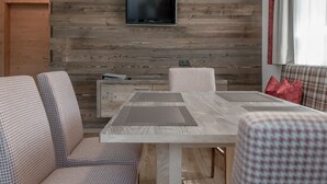 A modern room with a wooden wall, a flat-screen TV, a dining table with chairs, and a sofa with cushions. - The Peak Sölden by Interhome (Sölden)
