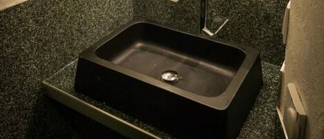 A bathroom with a black sink, granite countertop, and a mirror with lights above it.
