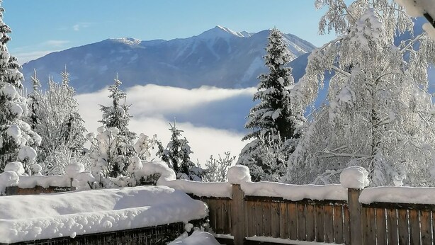 Eine verschneite Landschaft mit Holzzaun und Steinmauer.