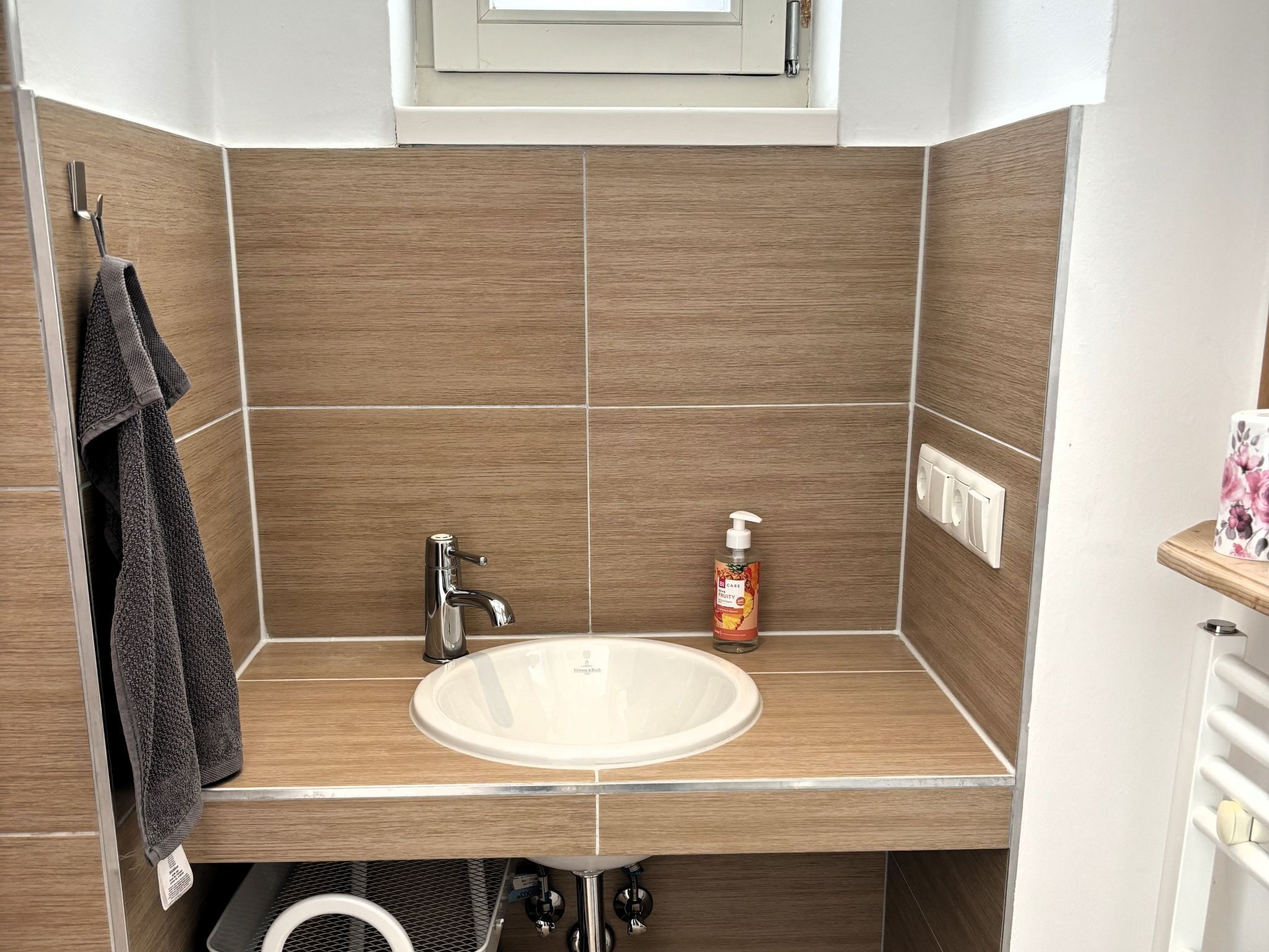 A bathroom with a white sink, wooden tiles, a towel rack, and a bottle of hand soap.