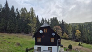 Ein rustikales Holzhaus mit geneigtem Dach, einer Satellitenschüssel und einer kleinen Terrasse mit Bänken.