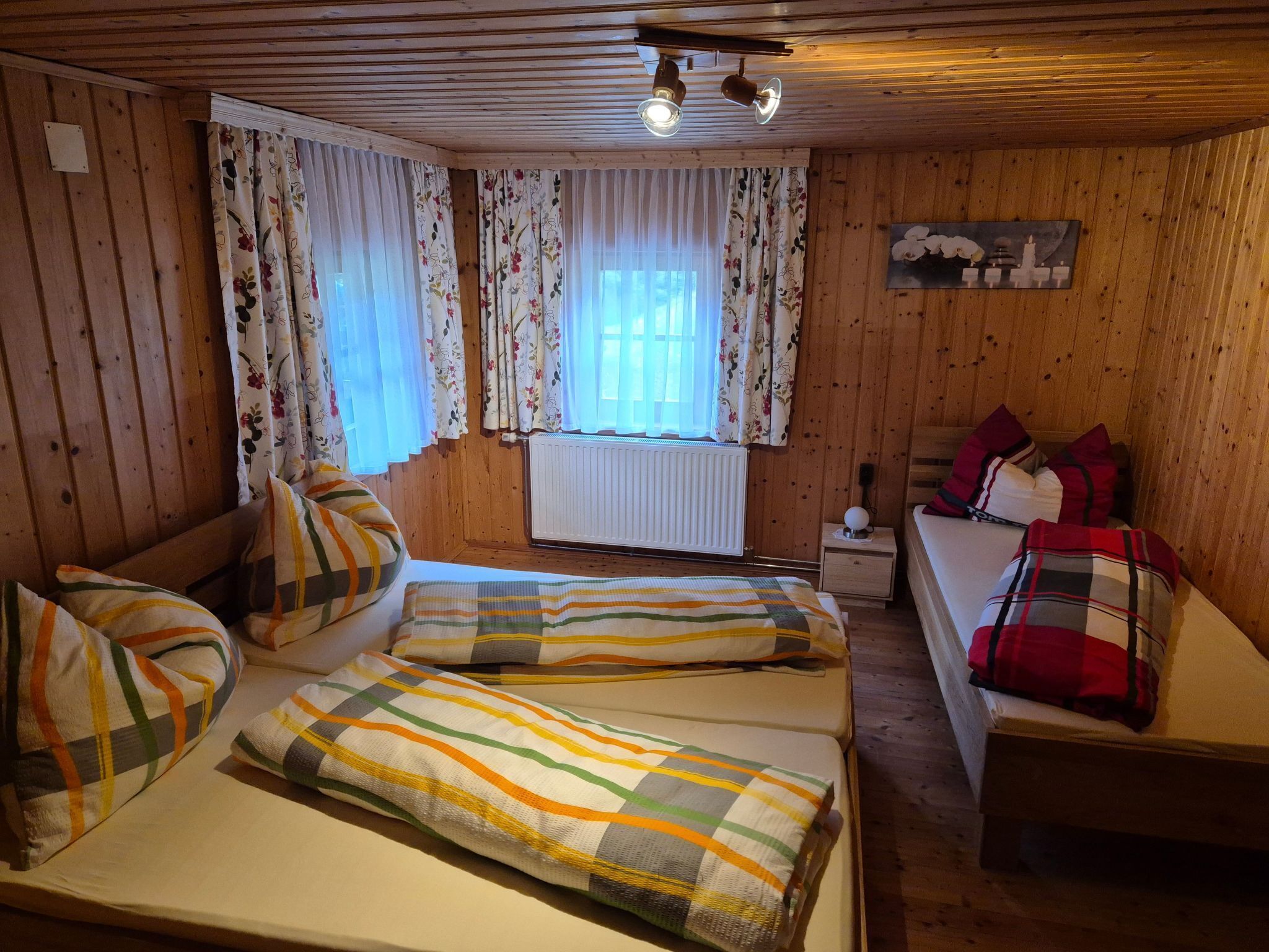 Una habitación acogedora con dos camas, paredes de madera, un radiador y una ventana con cortinas florales.