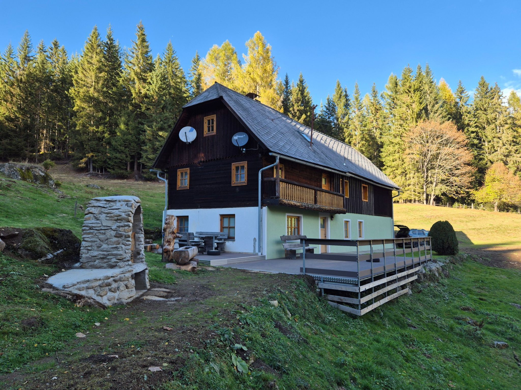 Una casa de madera rústica con antenas parabólicas, una estructura de piedra y una pequeña zona de estar al aire libre.