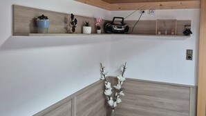Ein Eckzimmer mit Holzboden, einer weißen Wand, einem Holzschrank, einem Regal mit Dekoration und einem flauschigen Teppich.