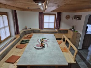 Una habitació acollidora amb una taula llarga, seients amb coixinets i una finestra amb persianes.