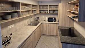 Eine kleine Küche mit Holzausstattung, einer eingebauten Mikrowelle, einem Spülbecken und Regalen mit Gläsern und Geschirr.