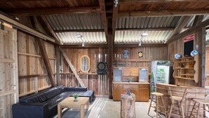 Ein rustikales Interieur mit Holzbalkendecke, einer Couch, einem Couchtisch, einer Bar und einem mit Getränken gefüllten Kühlschrank.