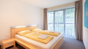 A modern hotel room with a large bed, a bedside table, and a view of the outdoors through large windows. - Bohemia 3 in Gargellen by Interhome (Gargellen)