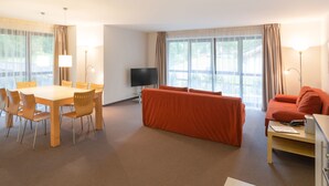 A modern hotel room with a dining area, a sofa, a TV, and large windows. - Bohemia 3 in Gargellen by Interhome (Gargellen)