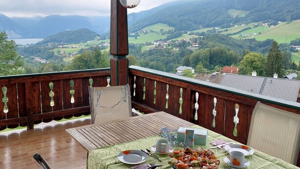 Un balcón con una mesa dispuesta para una comida, con vistas a un paisaje montañoso.