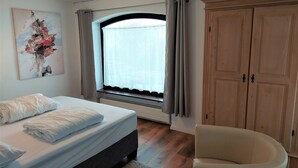 Un dormitorio con cama, cortinas en la ventana, un armario y una silla.