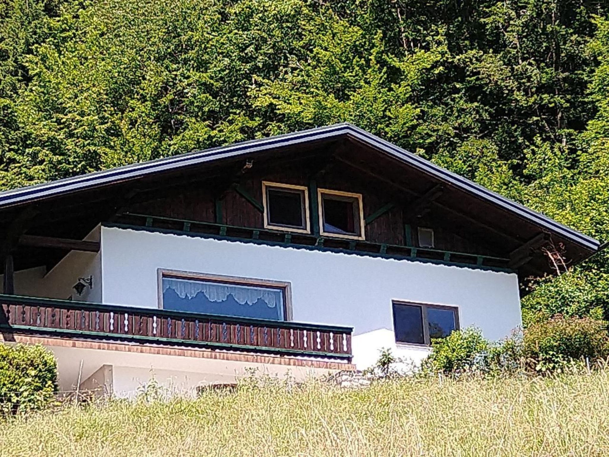 A two-story chalet with a balcony, surrounded by forest.