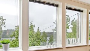 A room with three large windows, each with a view of greenery and a body of water.