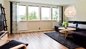A modern living room with a black sofa, a round coffee table, and a large window with a view of greenery.