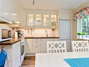 A modern kitchen with white cabinetry, a microwave, and a sink. There is a window with a view of trees and a decorative curtain.