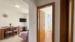 Een moderne woonkamer met een houten eettafel, een bank en een aan de muur bevestigde televisie.