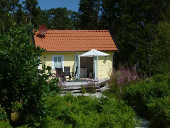A yellow house with a red roof, a satellite dish, and a covered patio with outdoor furniture. - Tiny house Gotland by Interhome (Ljugarn)