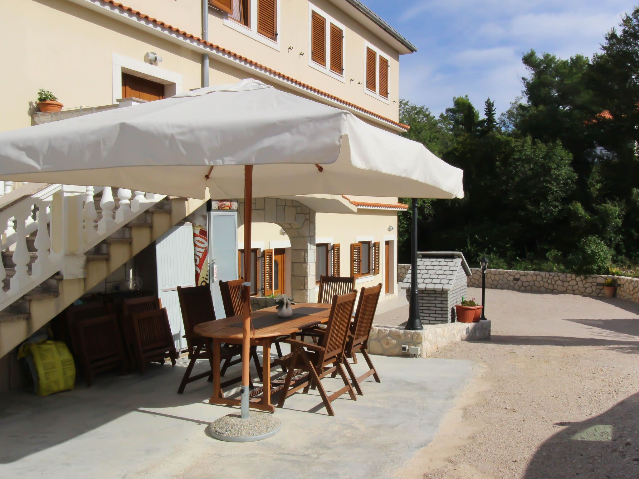 Eine Terrasse im Freien mit Tisch und Stühlen unter einem großen Sonnenschirm, einem Steinkamin und einer Treppe, die zu einer zweiten Etage führt.